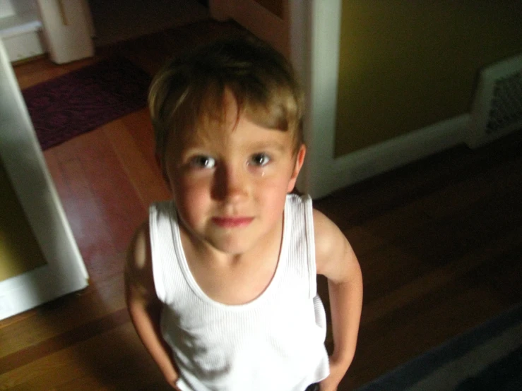 a young child in a white vest holds his hands on the hips of a red chair