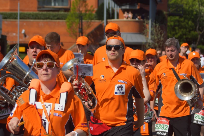 group of people in orange shirts marching a street with flags and musical instruments