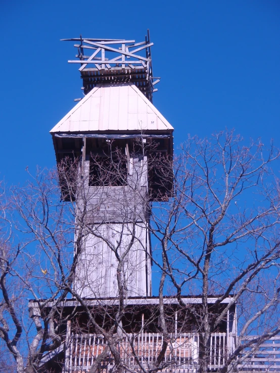 a tall tower with a weather vane sitting above some bare trees