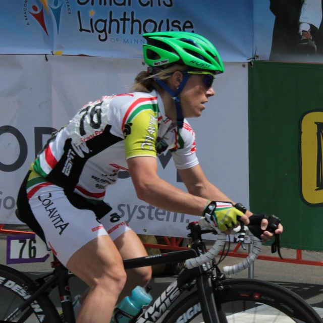 a man with a green helmet and white and black shirt riding a bike down the street