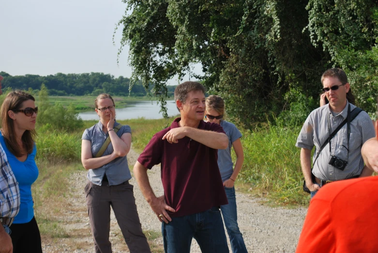 a group of people stand around and watch a man pointing to the side of the street