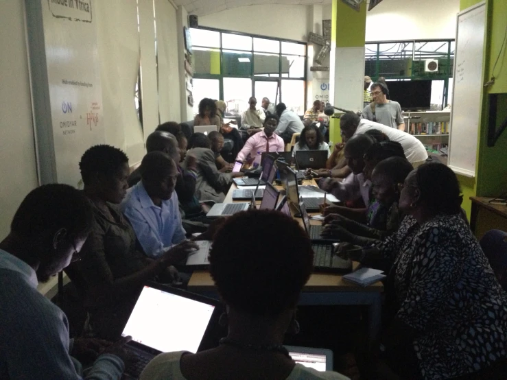 a group of people are gathered around table with laptops