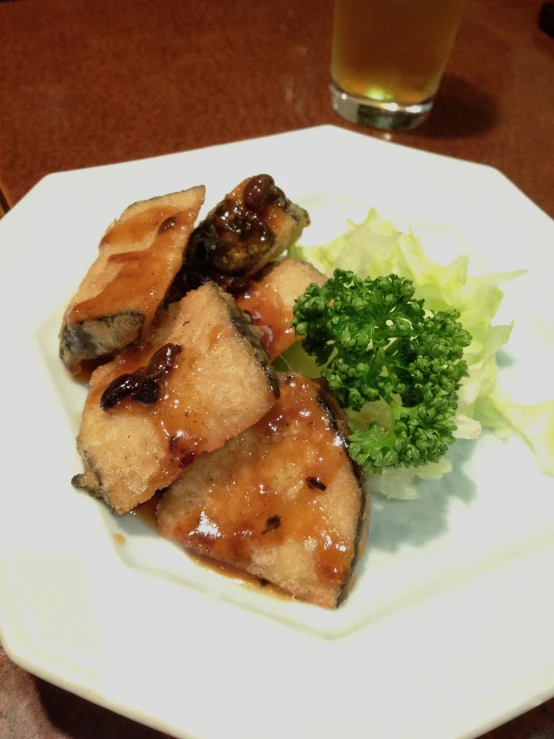 a plate topped with meat and broccoli next to a glass of beer