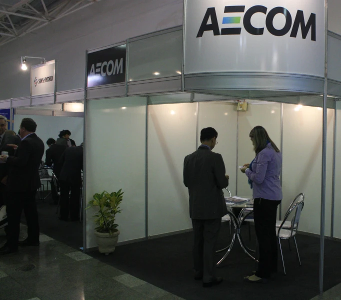 people standing around a small exhibition booth with a woman talking