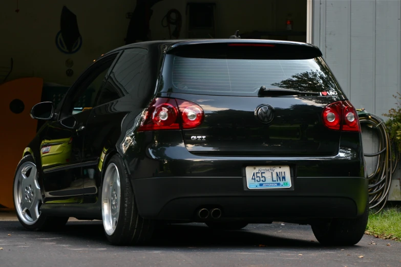 a black car with its back lights turned is parked in front of a garage