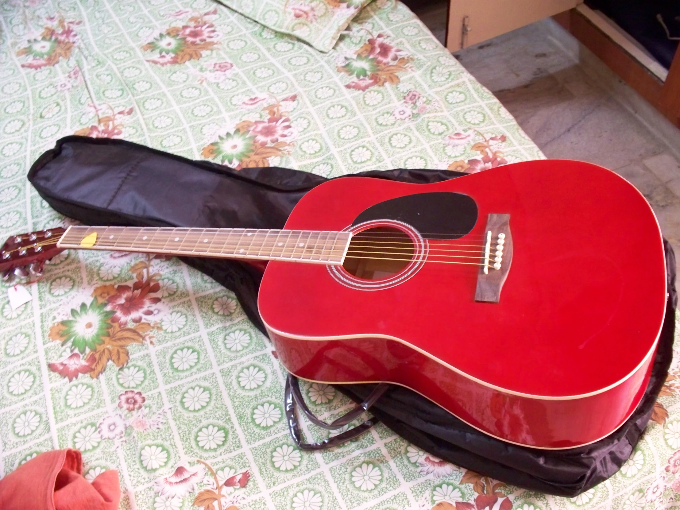 a red guitar sitting on top of a bed next to a bag