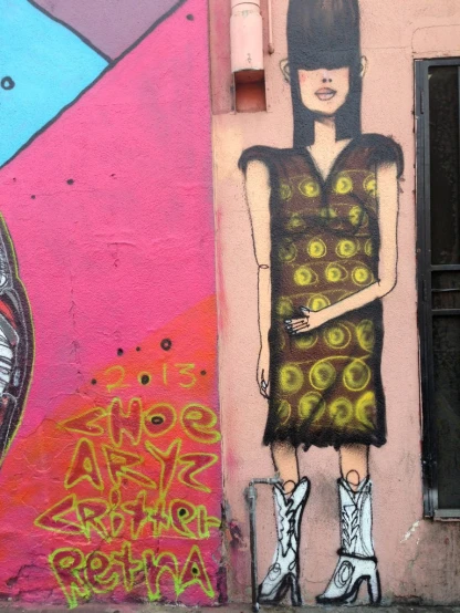 the wall is covered in colorful graffiti and there is a young woman in boots wearing a dress