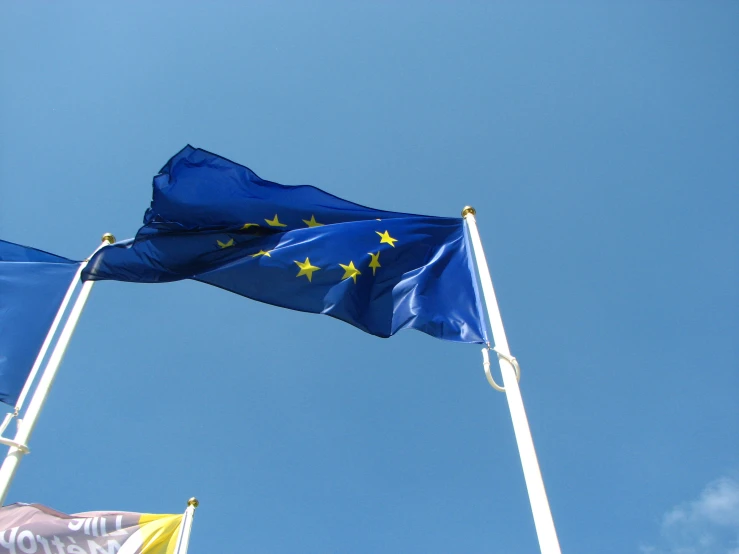 two flags against a blue sky with a writing below them