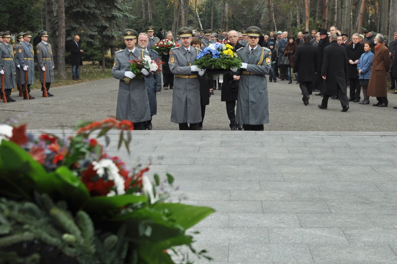 three men in grey uniforms stand at a wreath