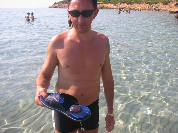 a man in a bikini holding a boogie board and sunglasses on his chest