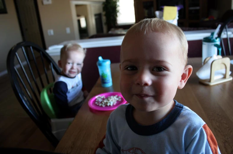 two boys sitting at a table eating cereal
