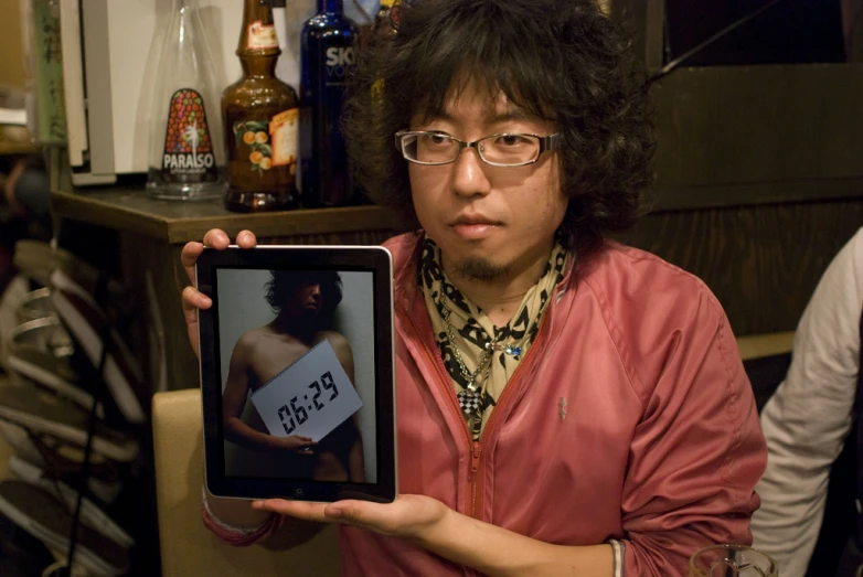 the man holds up a tablet with an image of a man with his shirt pulled back