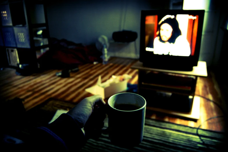 a person holds a coffee cup and watches tv in the living room