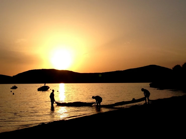 some people are standing on the water and at sunset