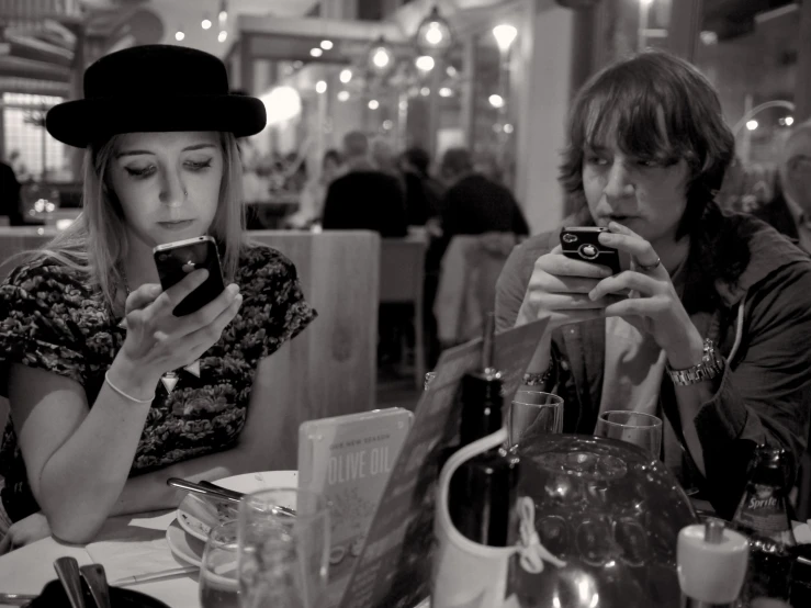two people sitting at a restaurant table with one looking at their phones