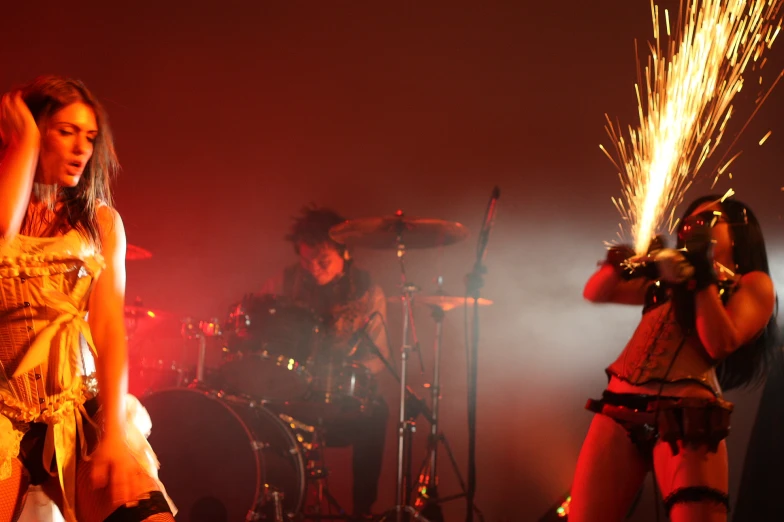 two women in costumes, with their hands on their hips, standing on stage and performing with a man behind them