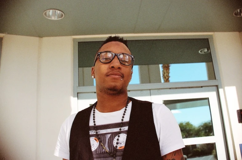 man standing in front of open window wearing glasses and a black vest