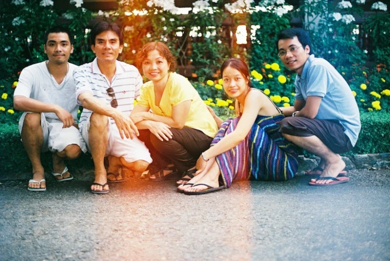 four people sitting on the curb next to yellow flowers