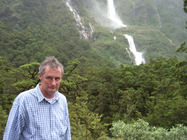 a man with white hair standing in front of a waterfall