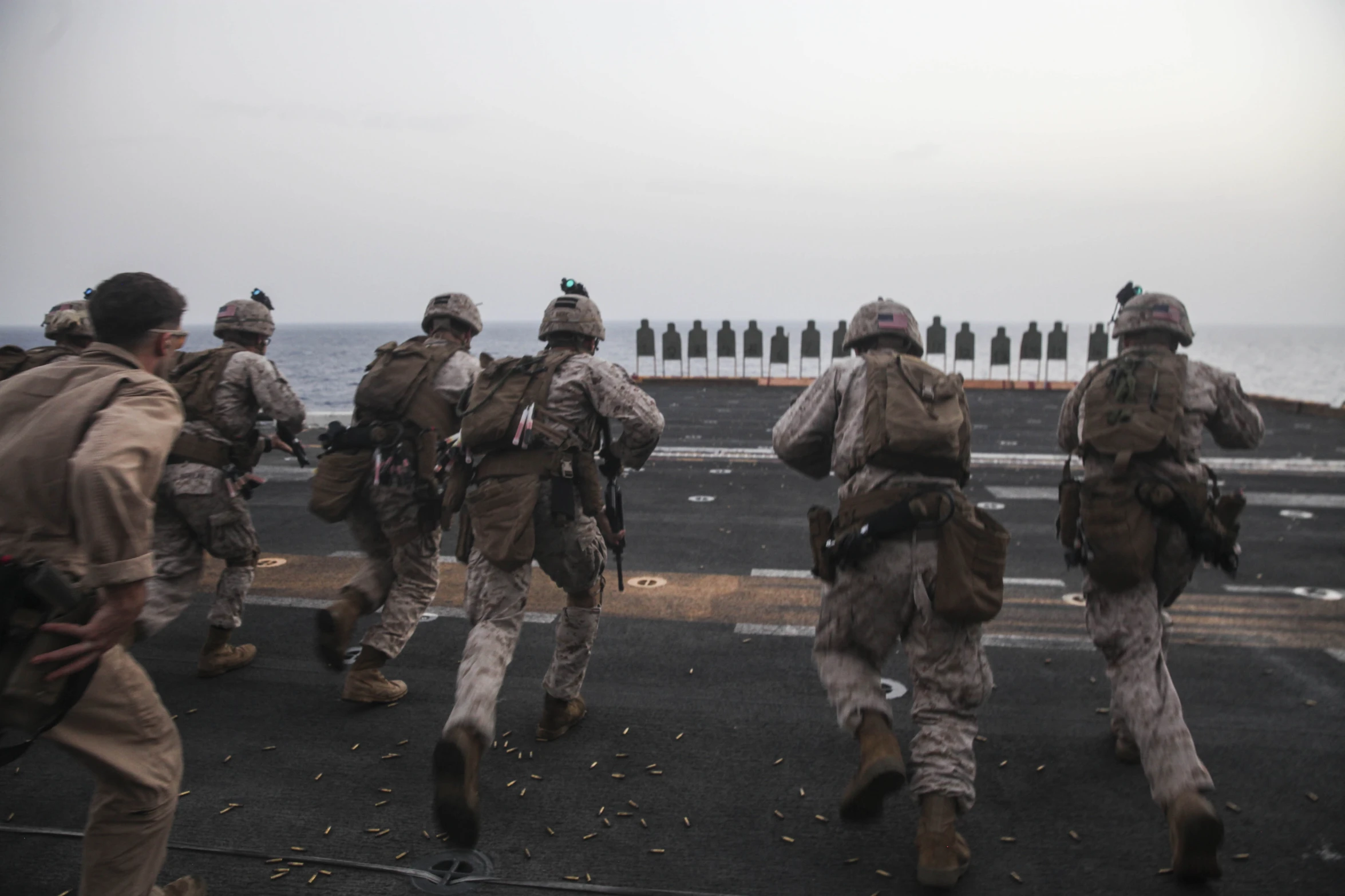 marines in full gear are running along a military ship