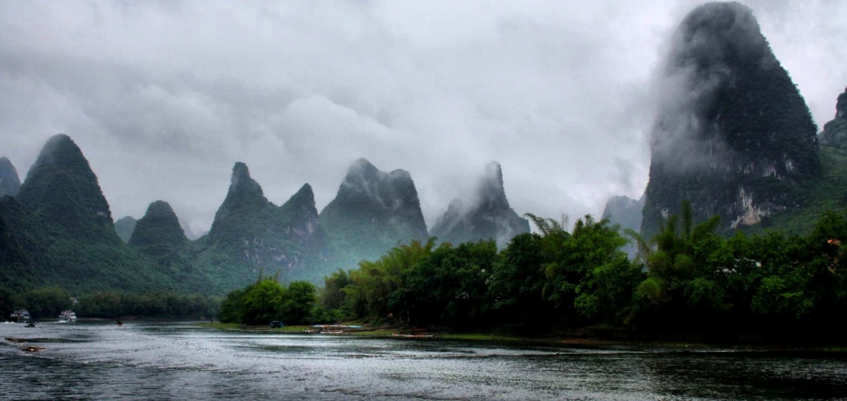 mountains and river covered in mist, with boats parked on them