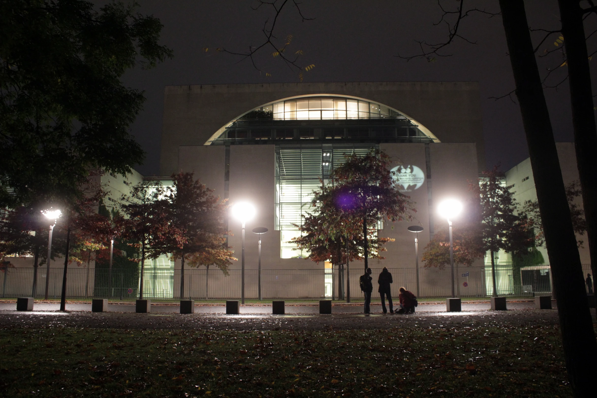 three people standing on a curb with the building lit up behind them