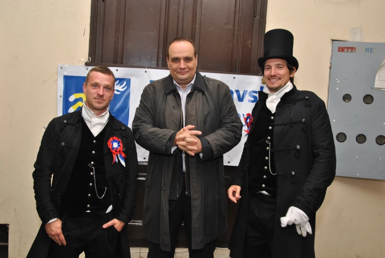 three men in colonial garb standing with a man in top hat and jacket and another man in vest and tie