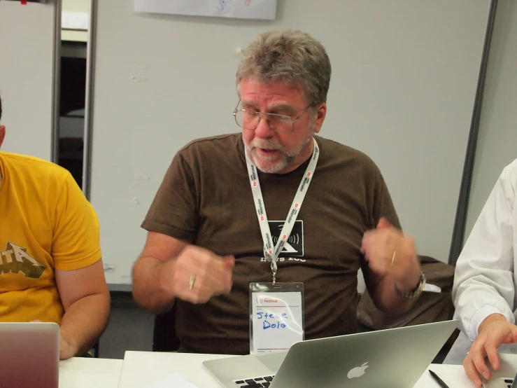 three men sit at a table with a laptop in front of them