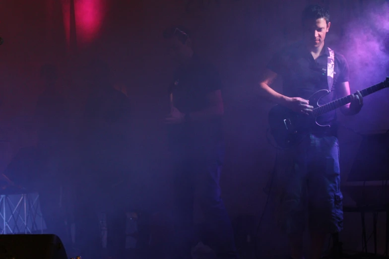 the guitarist is standing in a smoke filled room