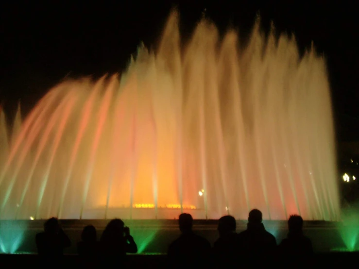 many people standing in front of a fountain at night