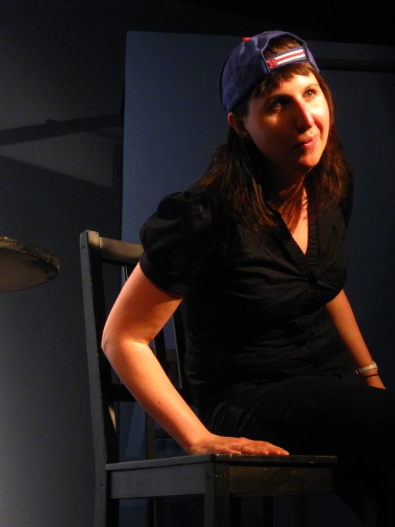 a woman sits in a chair with a baseball cap on