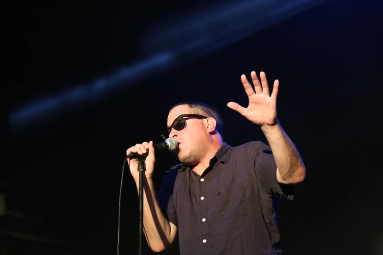 a man in black shirt with a microphone and hand up
