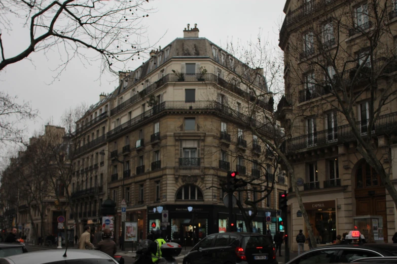 many cars driving on a busy street with an apartment building on the corner