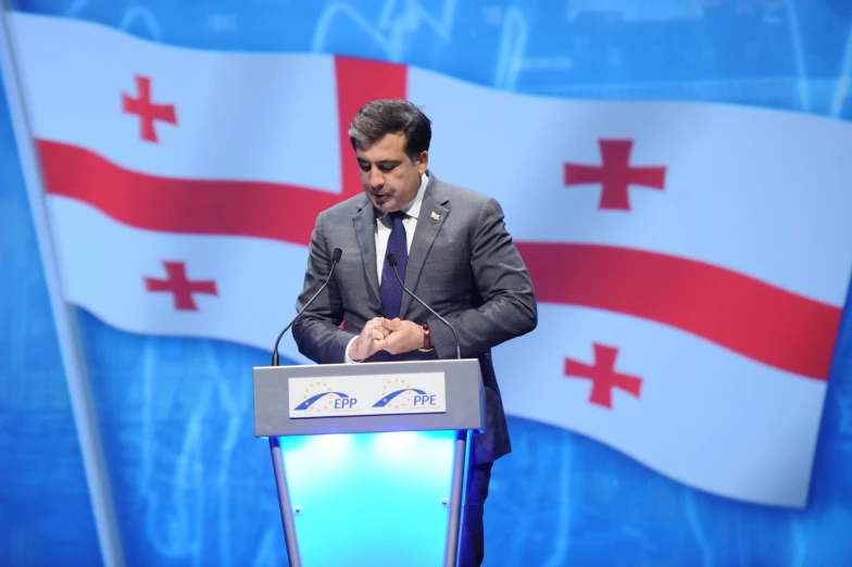 a man speaking on the stage and with an ice flag behind him