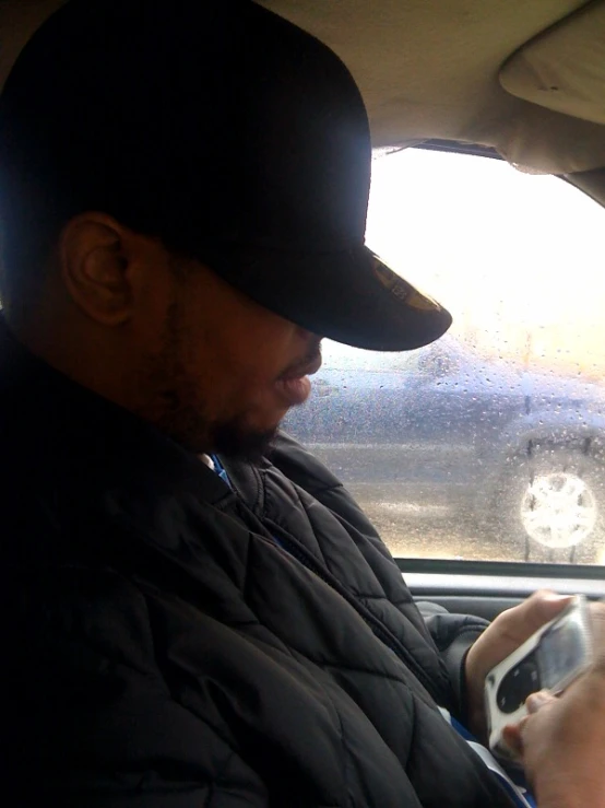 a black man sitting in a car looking at his cell phone