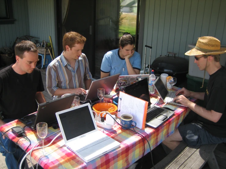 four people sitting at a table with laptops