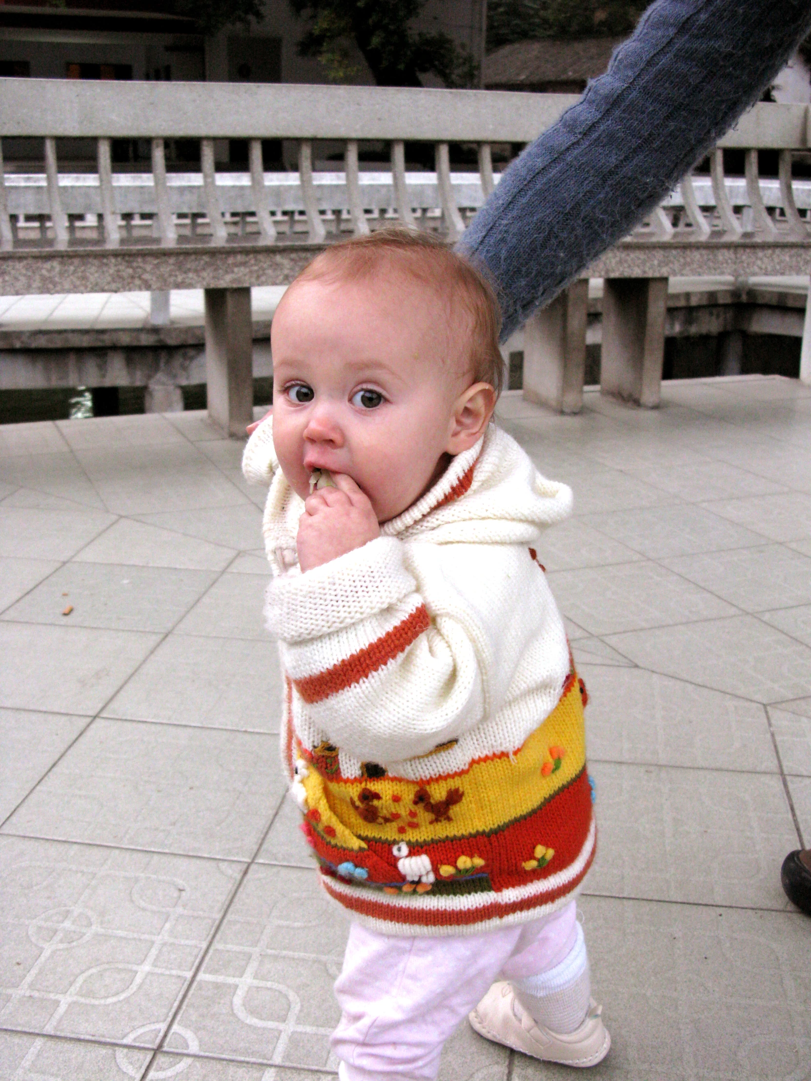 a small child with a sweater standing on some bricks