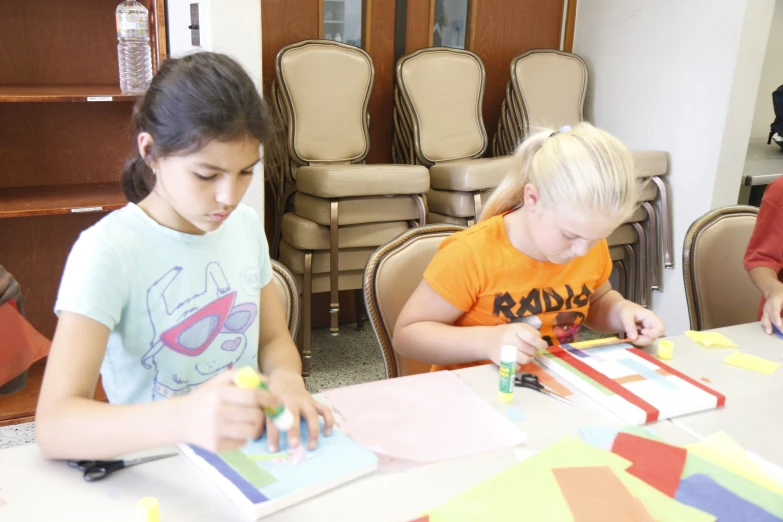 a couple of s sitting at a table doing crafts