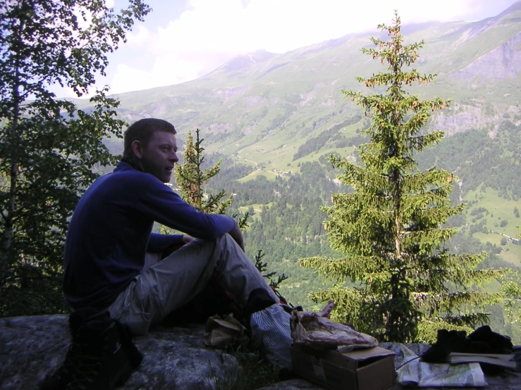 a man sitting on the edge of a mountain with a bag of food