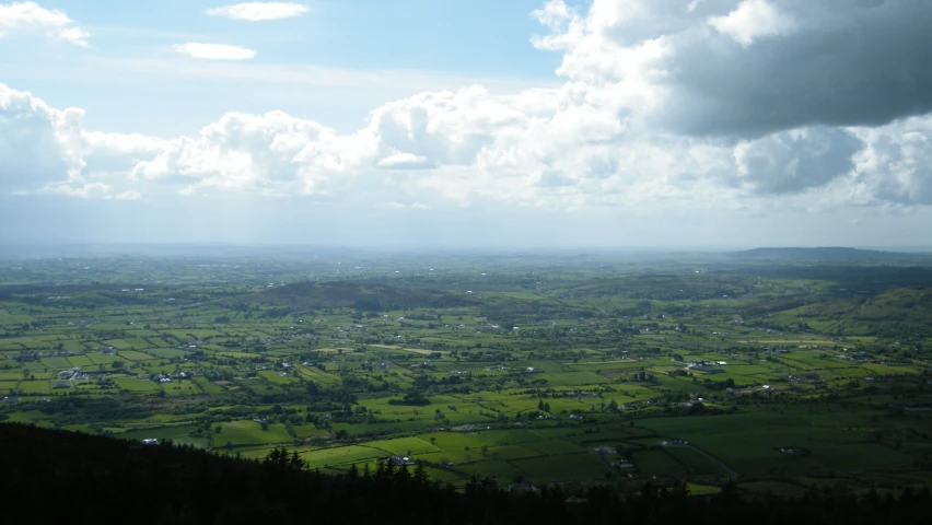 an aerial view of a lush green plain and a cloudy sky
