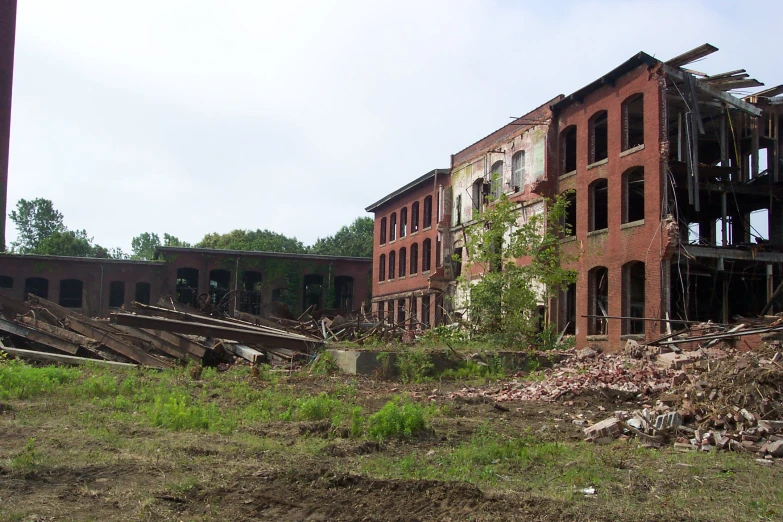 a large brick building with broken windows, sitting next to a forest