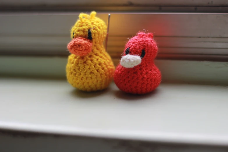 two crocheted little figurines sitting on a window sill