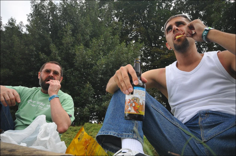 two men sitting together in the park having drinks