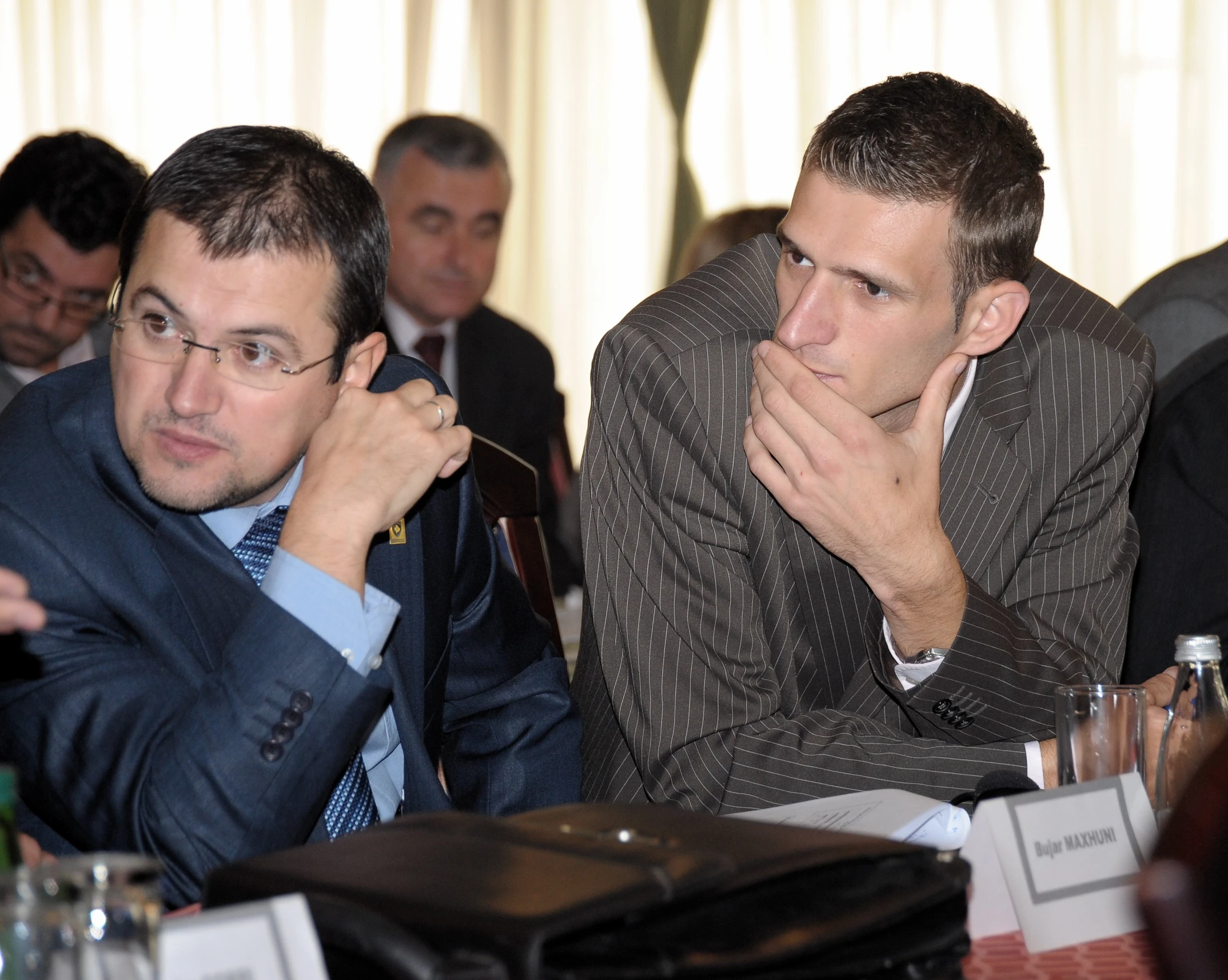 two men sitting at a table with other people in the background