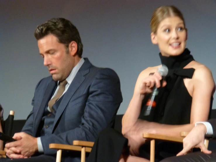 two people in suits sitting on chairs at an event