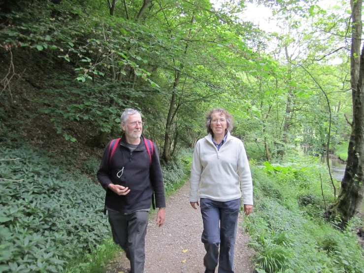 a man and woman walking down a path through the forest