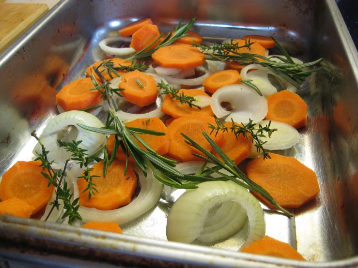 carrots and onions in a pan with rosemary on top