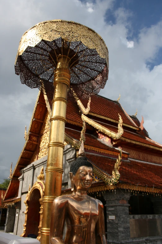 an image of golden statue with umbrella in front of a temple