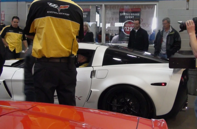 people and a car in a garage next to a woman taking a picture