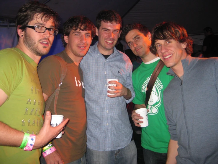 four young men smiling while holding cups of coffee